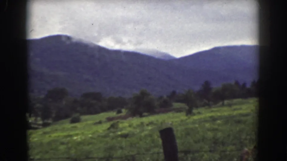 Late frame from a 1939 Mount Washington area pan, showing hillside grass, trees, a fence post, and purple-blue mountains under clouds.