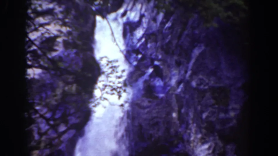1939 8mm Mount Washington view of a waterfall descending between shadowed rock faces and sparse plants.