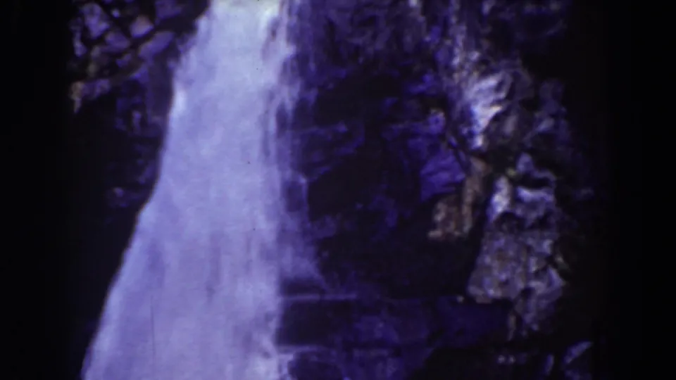 Aged 8mm frame of a waterfall plunging beside jagged Mount Washington rocks, with visible dark film borders.