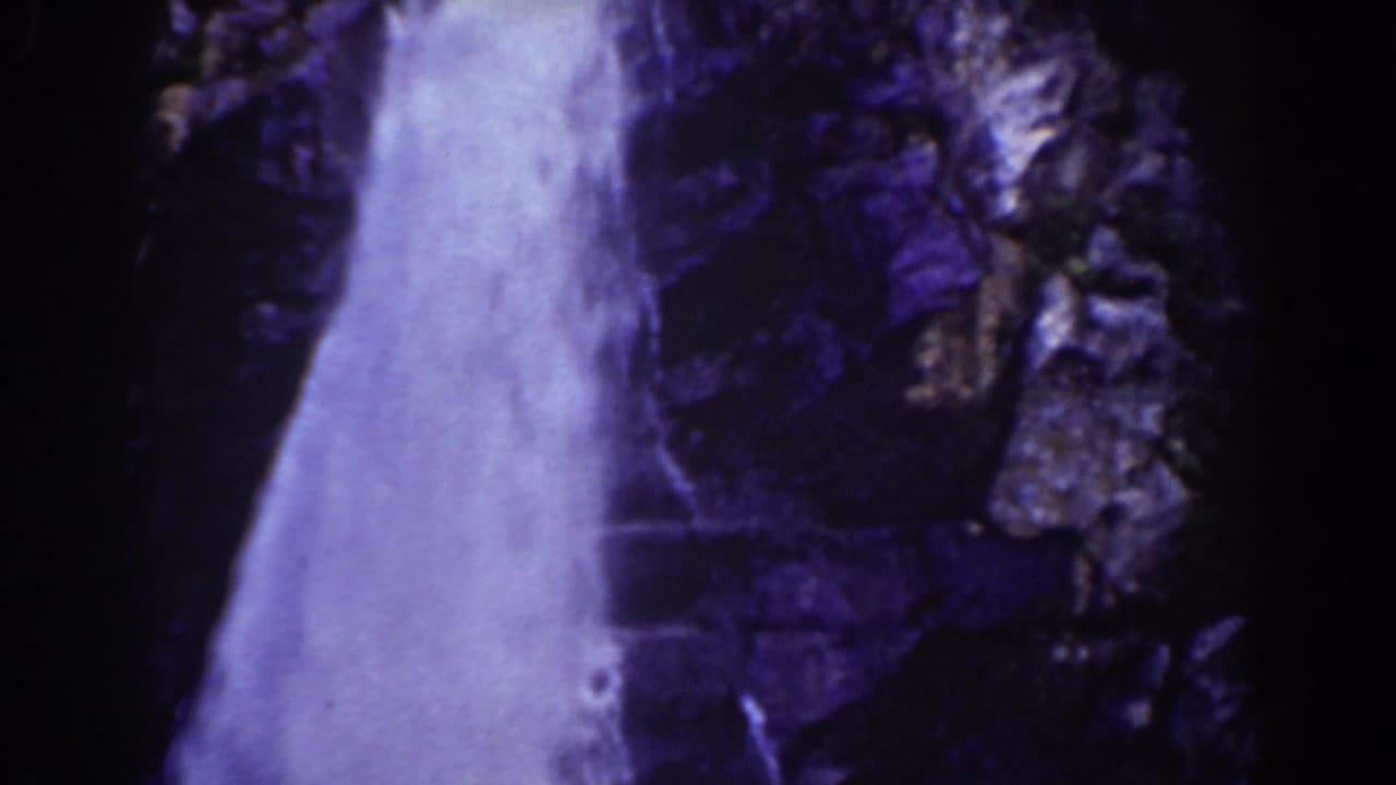 Waterfall dropping beside dark rock in a grainy 8mm frame.