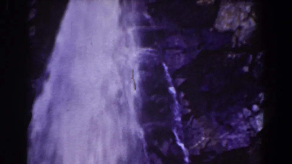 Vintage 8mm frame of the lower waterfall section with misty white water and dark purple-shifted rocks.