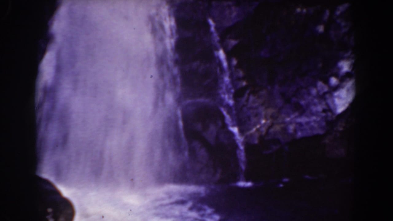 1939 Mount Washington home-movie frame showing a small waterfall, dark rock wall, and foamy water below.