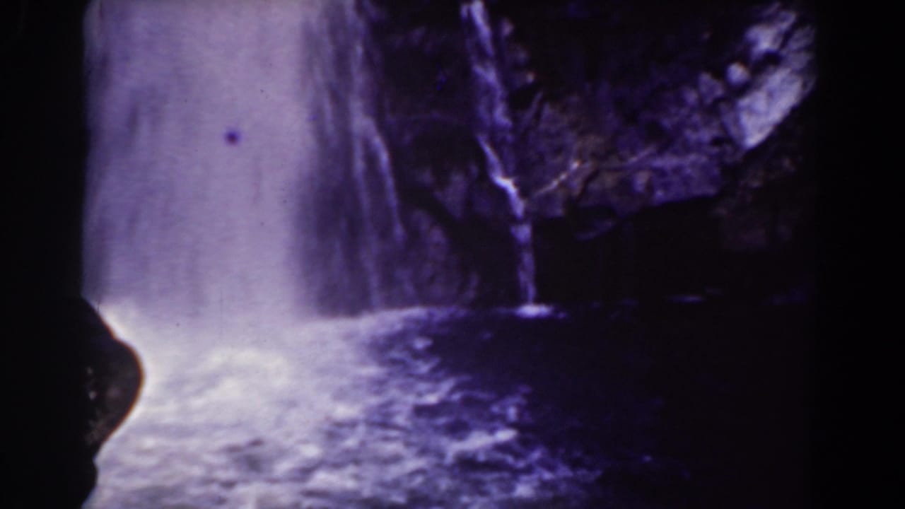 Waterfall and foamy pool framed by dark rock on both sides.