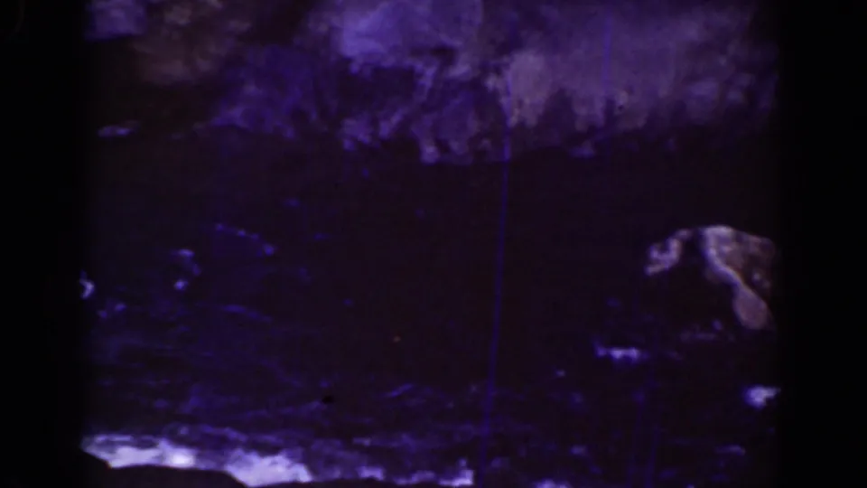 1939 8mm Mount Washington footage showing a dim rocky stream area with dark stones, shallow water, and blue-purple film color shifts.