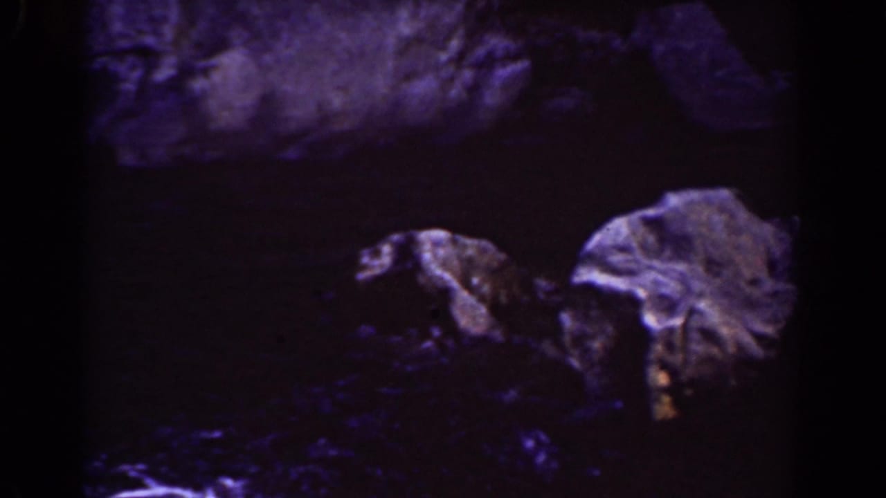 Rocky watercourse with pale stones and dark pools under dim exposure.