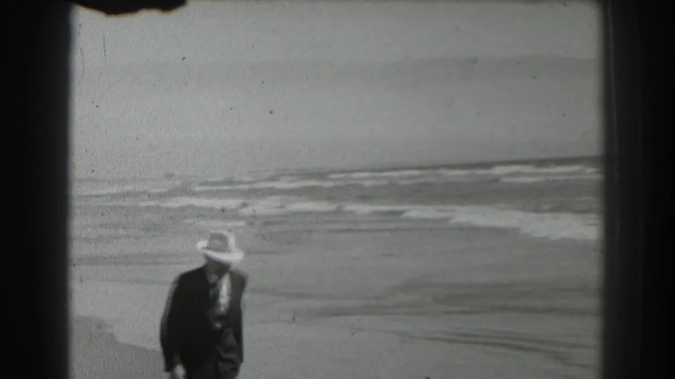 Near the end of the shot, the man in formal clothing moves through the lower frame against the beach and surf.