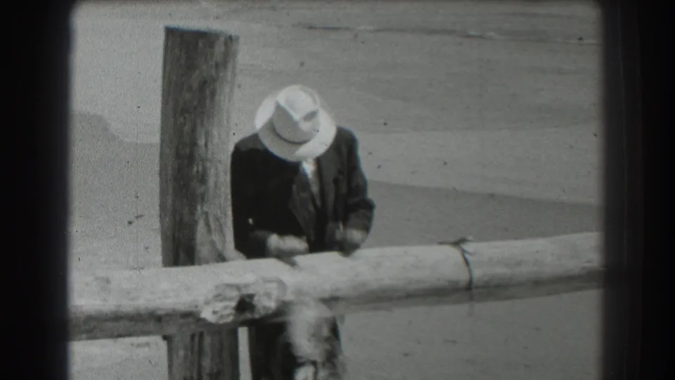The final frame shows the fedora-wearing man behind the rail, looking down near a tied rope with the beach and water behind him.