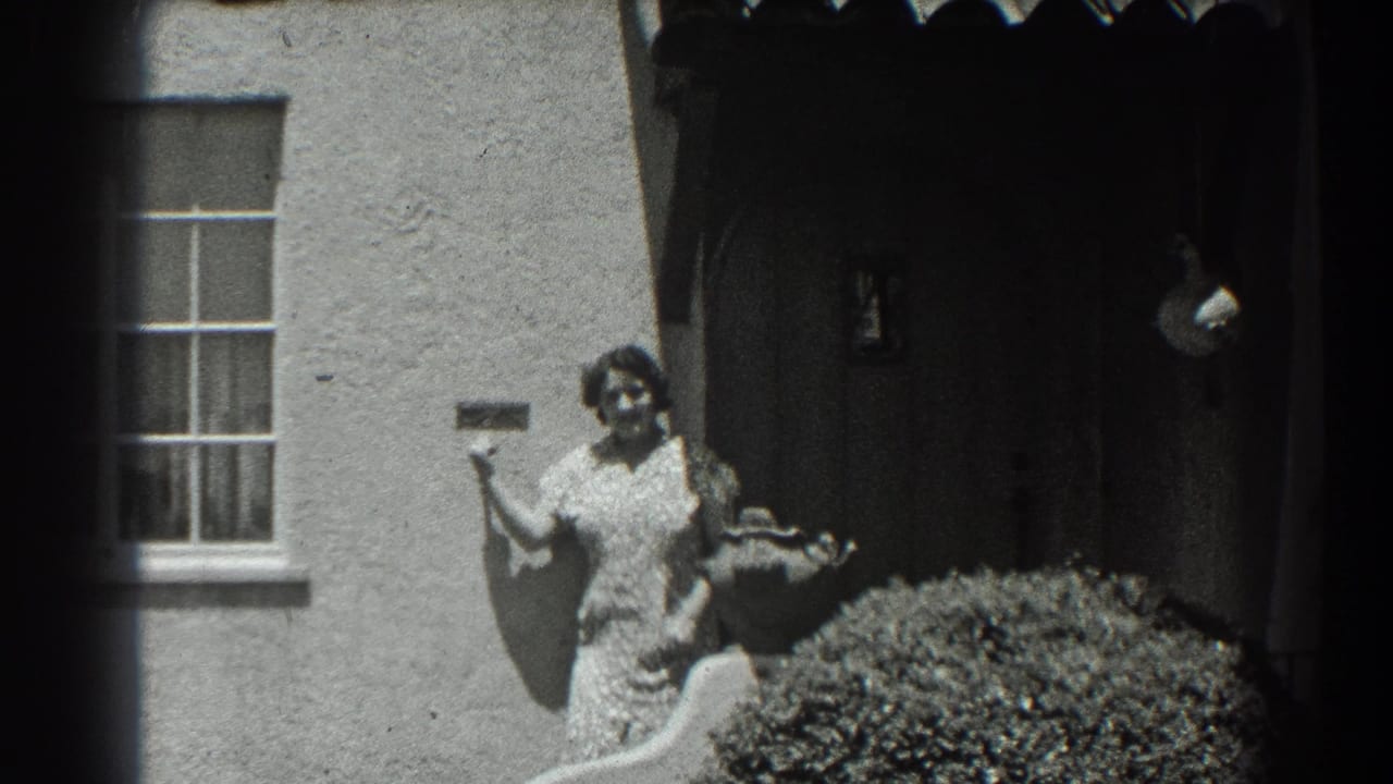 Woman faces the camera near a stucco house entry, with a shrub in front.