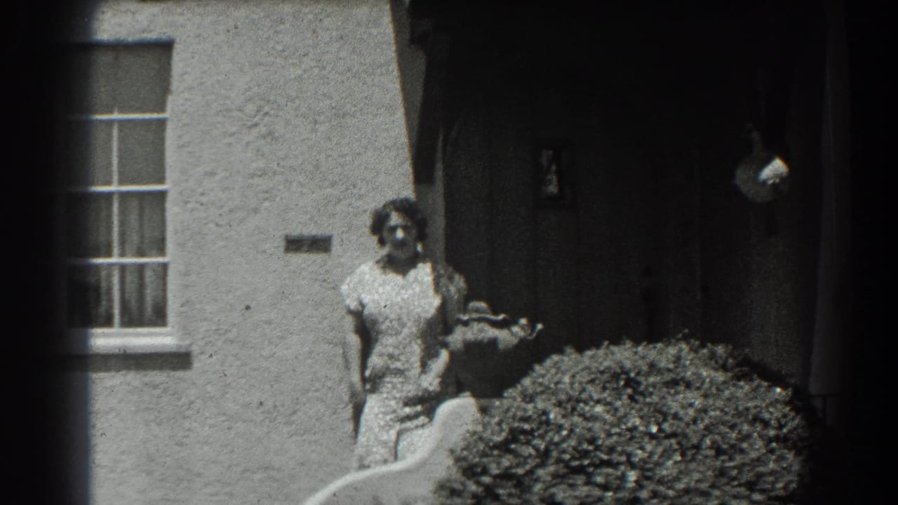 In supported 1939 San Francisco home-movie footage, a woman stands near a stucco house entry beside a window and shrub.