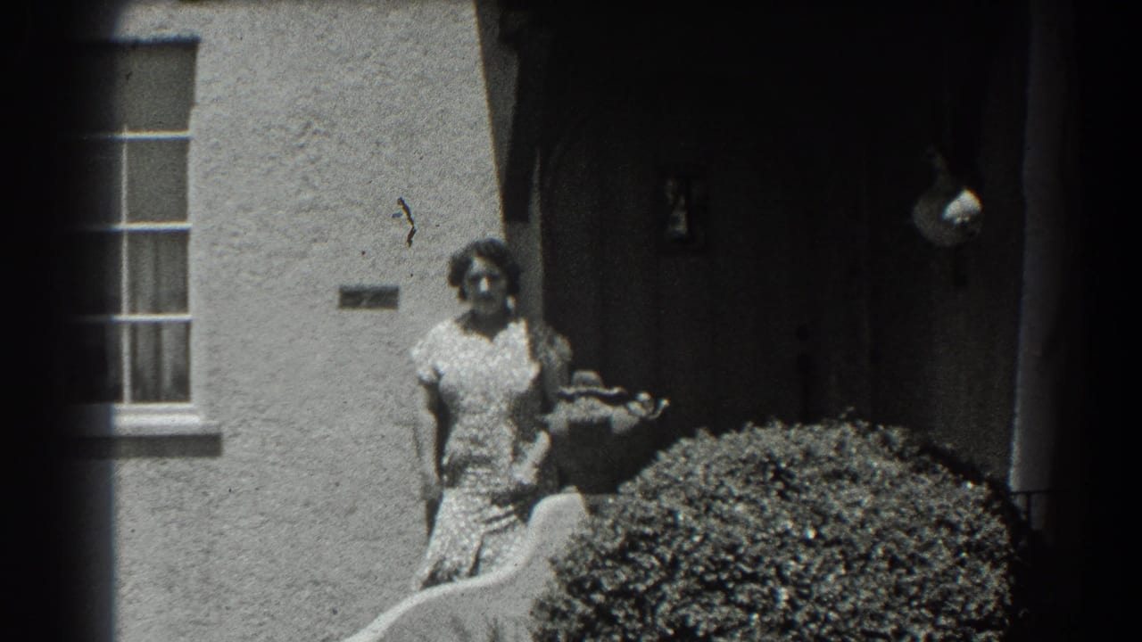 Woman standing in front of a stucco house beside a doorway and rounded shrub.
