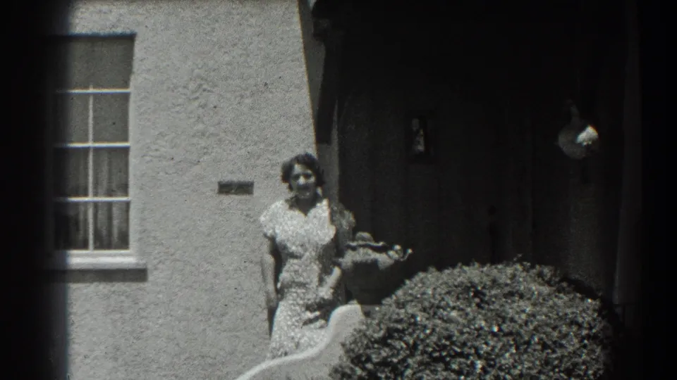 The home-movie frame shows a woman outside a San Francisco stucco house, with residential details and foliage visible.