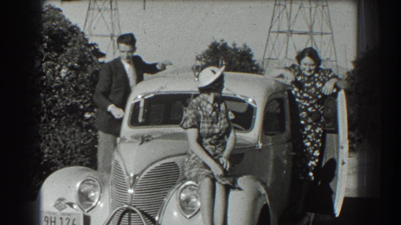 Three people pose around a rounded 1930s sedan outdoors.
