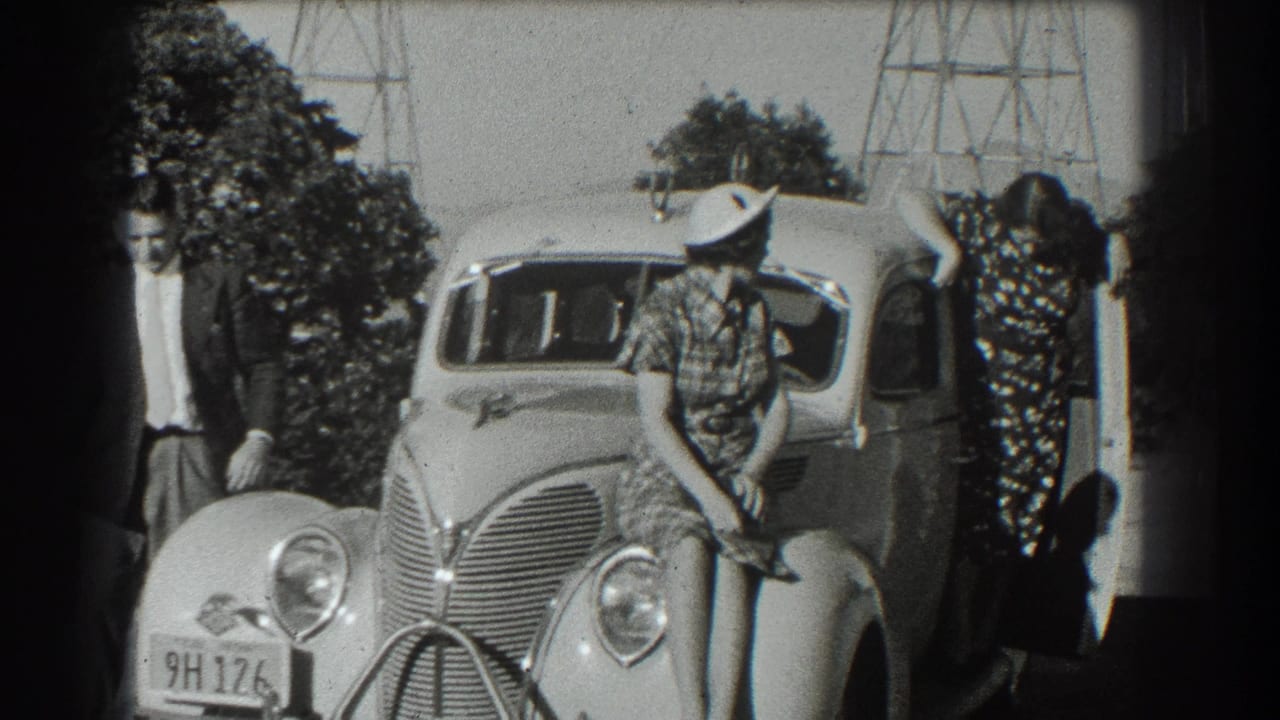 Group remains posed around the sedan as the woman raises an arm near the open door.