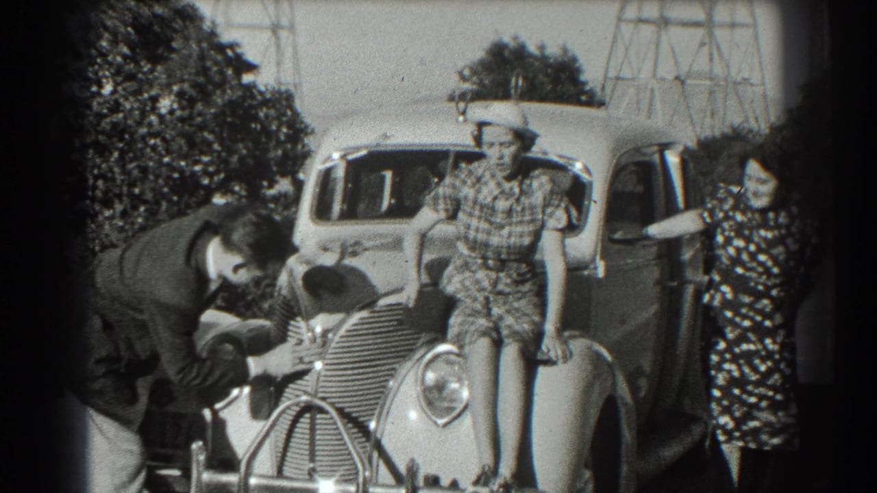 In 1939 San Francisco home-movie footage, a man bends over the front of a rounded car as two women in dresses and hats pose nearby.