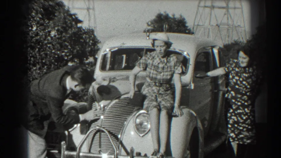In 1939 San Francisco home-movie footage, a man bends over the front of a rounded car as two women in dresses and hats pose nearby.