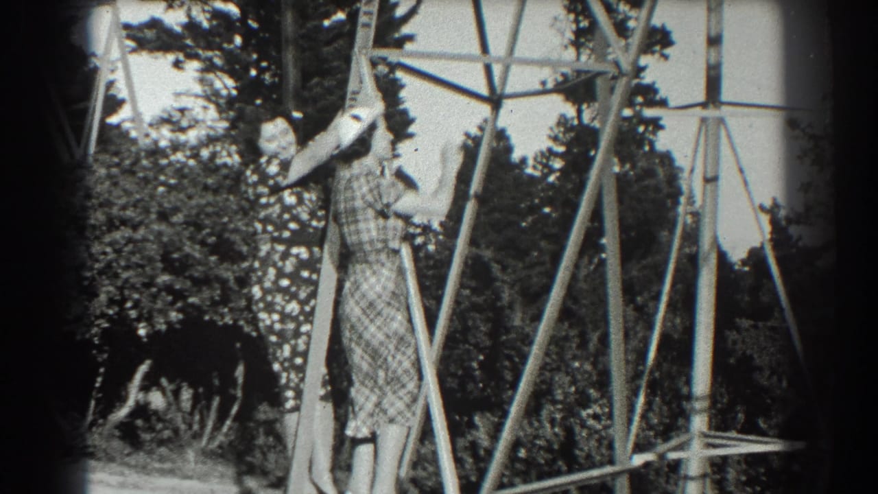 Woman in a plaid dress climbs a metal pylon while another woman stands nearby.