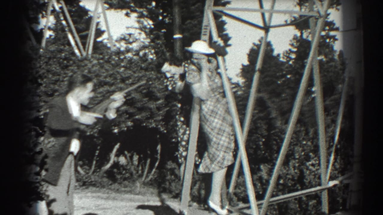Man in a suit points a toy gun toward a woman in a plaid dress on a wooden frame.