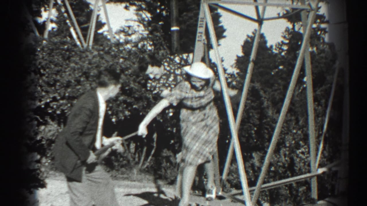 Man crouches while pointing a toy gun as a woman on the wooden frame reaches out.