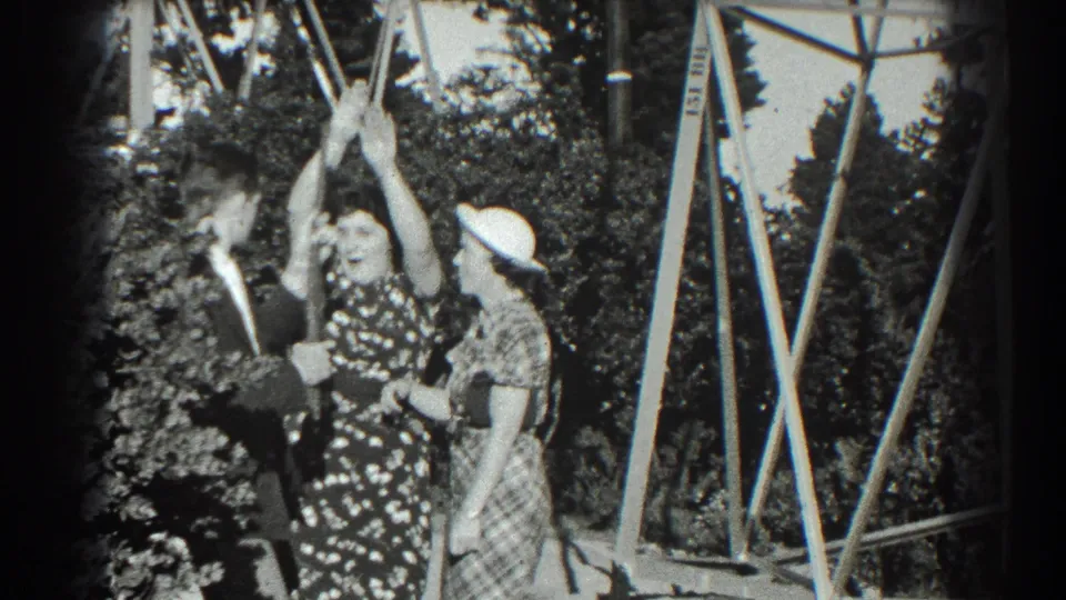In the San Francisco park setting, the woman in a floral dress raises her arms as the suited man and hat-wearing woman continue the playful scene.