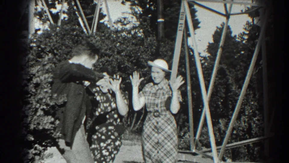 The suited man leans into the playful exchange as both women hold their hands up in the 1939 San Francisco home-movie scene.