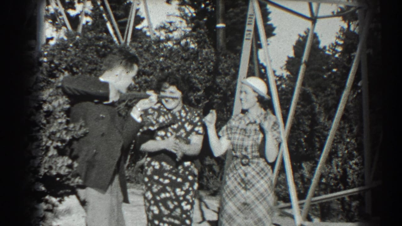 Three adults stand in a sunny garden near a metal trellis, reacting playfully.