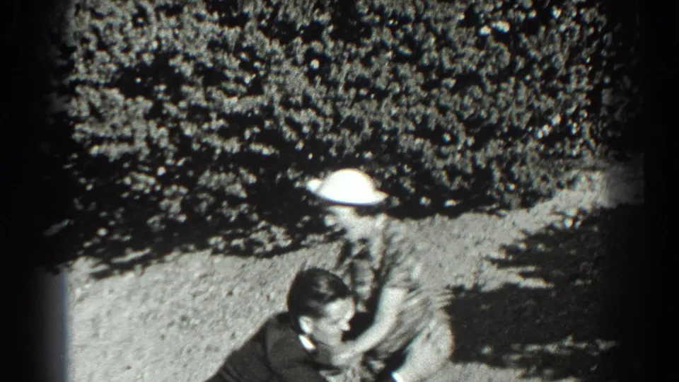 In 1939 San Francisco home-movie footage, a woman in a plaid dress and white hat approaches a man on a bright hillside.