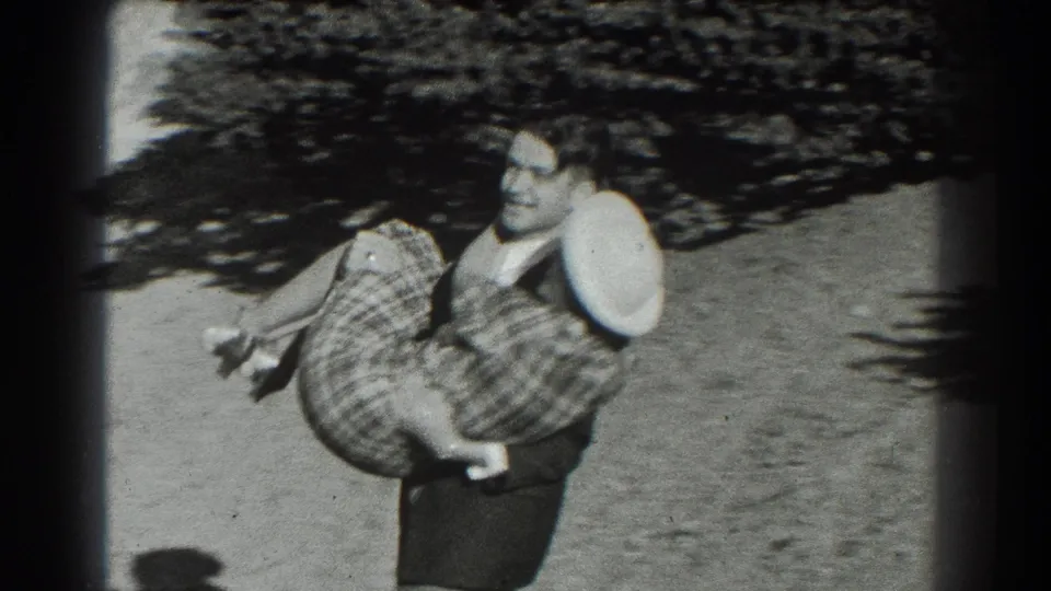 A man in a dark suit holds the woman in a plaid dress and white hat during an outdoor embrace in San Francisco, 1939.