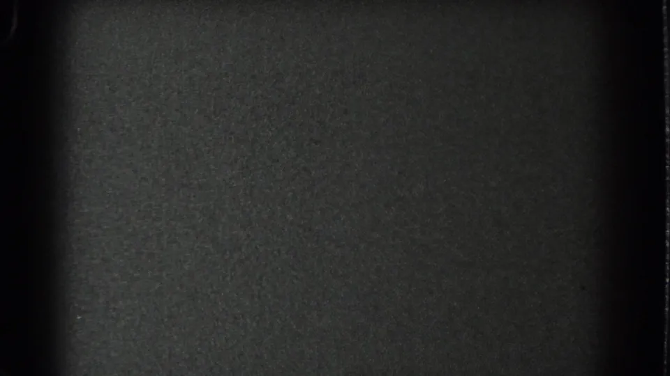 Underexposed 8mm frame from the San Francisco clip, showing mostly dark film texture and a vertical obstruction before the bay view appears.