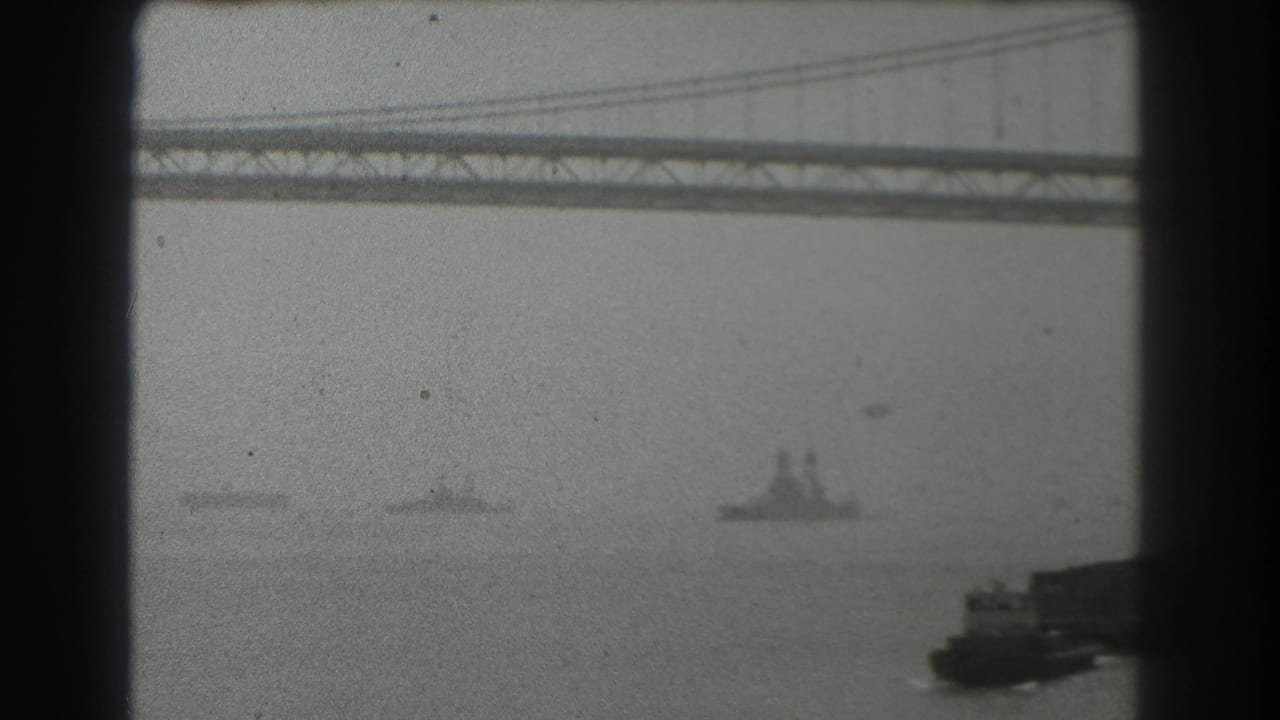 1939 San Francisco bay view with the Bay Bridge crossing the upper frame and several ships moving through haze below.