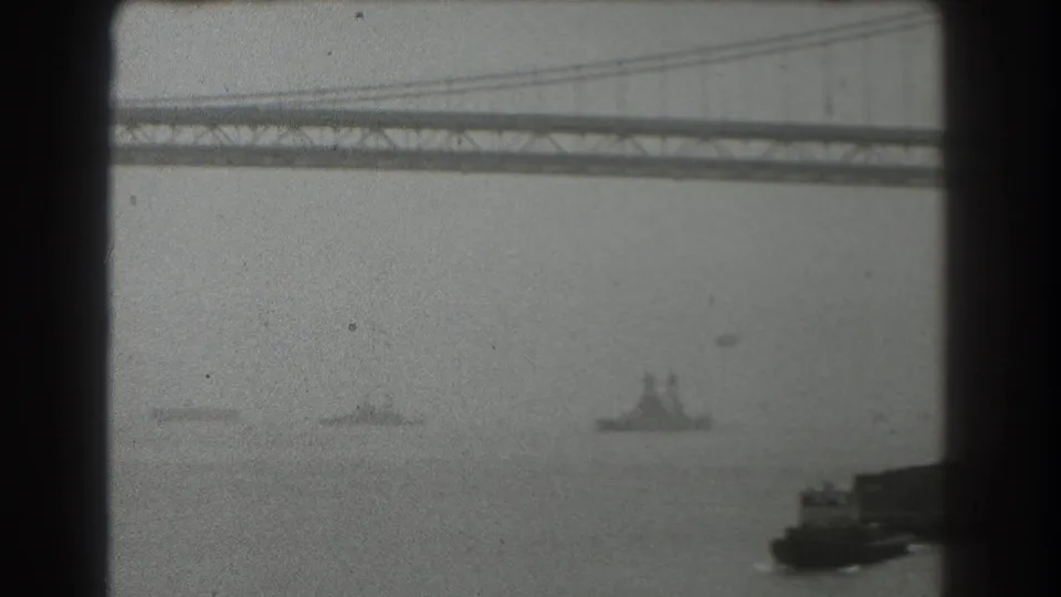 1939 San Francisco bay view with the Bay Bridge crossing the upper frame and several ships moving through haze below.