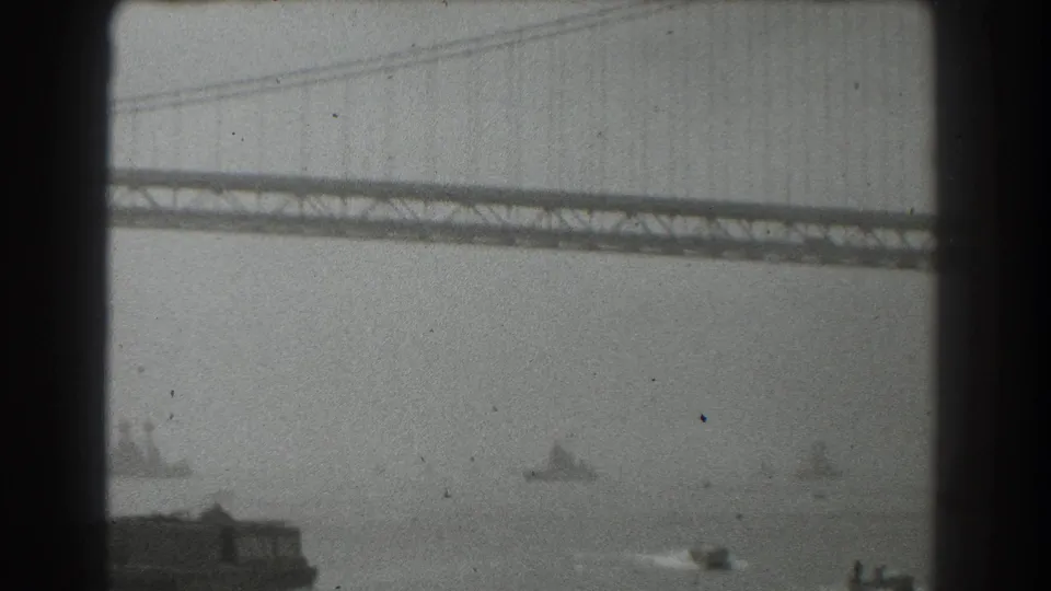 Late-1930s San Francisco bridge view with the span cutting across the frame and multiple vessels faintly visible on the bay.