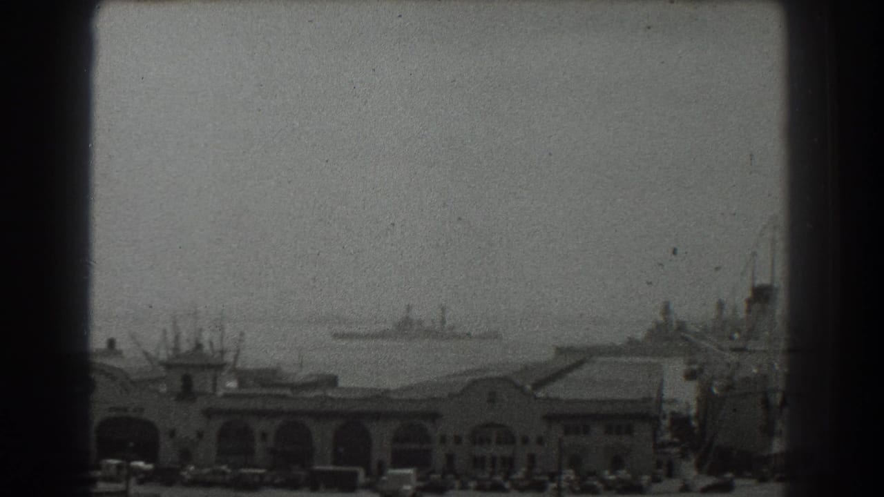 Hazy harbor view with arched waterfront buildings, distant ships, and a large vessel at right.
