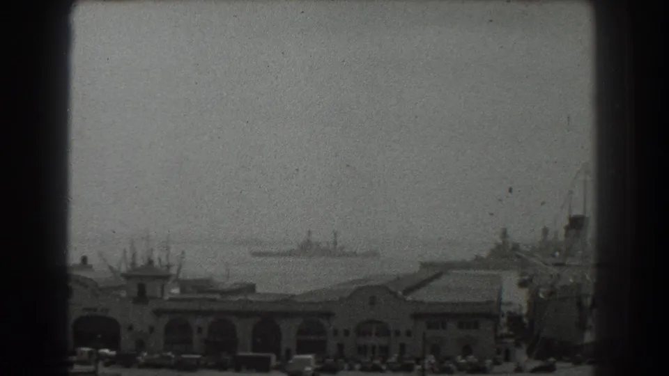 1939 San Francisco harbor view with arched port buildings, distant bay ships, and a large docked vessel at the right edge.
