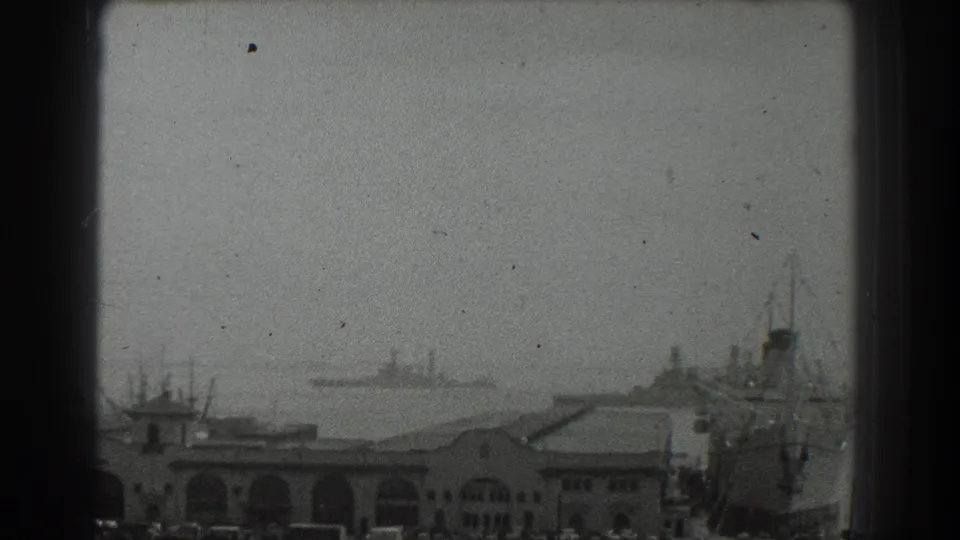 Static 1939 San Francisco waterfront frame showing arched port buildings, a large vessel, and distant ships in haze.