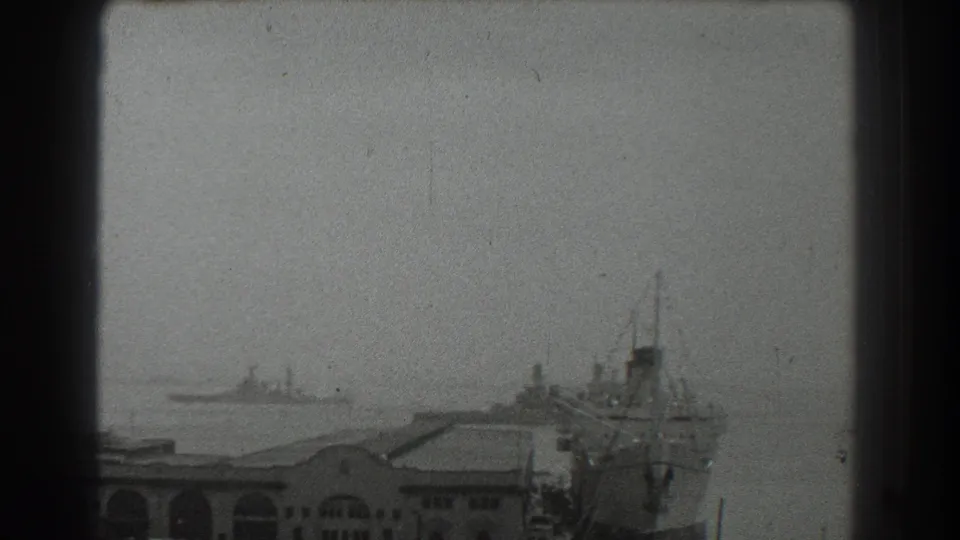 Grainy 1939 San Francisco bay view with port buildings, distant vessels, and a large ship docked on the right.