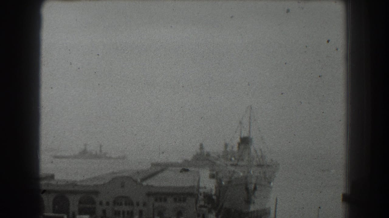 1939 San Francisco harbor view with a docked ship beside waterfront buildings and a distant vessel across the bay.