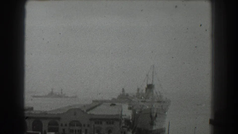 1939 San Francisco harbor view with a docked ship beside waterfront buildings and a distant vessel across the bay.