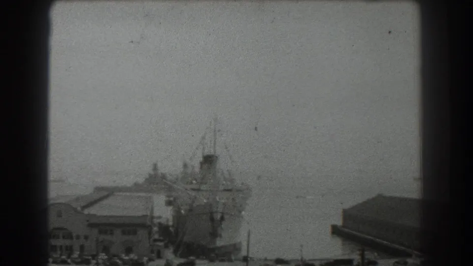 Soft 8mm frame of the 1939 San Francisco waterfront, with a docked ship, low harbor building, and open bay beyond.