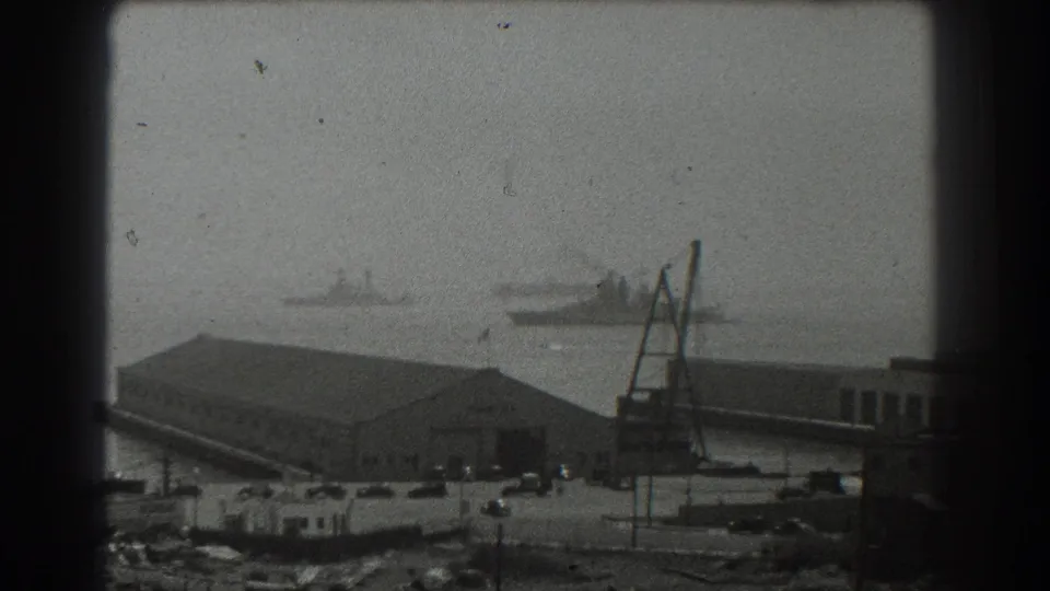 Wider 1939 San Francisco harbor view with industrial buildings, cranes, pier structures, and distant vessels on the bay.