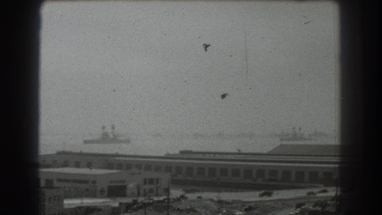 Hazy waterfront buildings with distant ships, seen through a dark window frame.