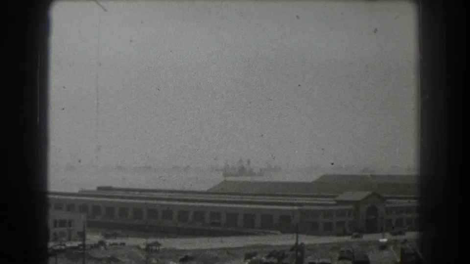 San Francisco waterfront scene from 1939, showing a long building facade, cars, and ships in haze beyond a dark vertical frame.