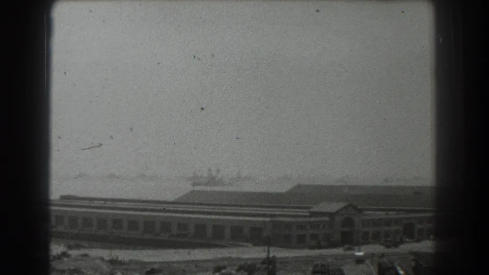 1939 San Francisco waterfront view with a long low building, parked cars, haze, and dark 8mm frame borders.