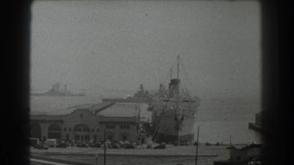 1939 San Francisco port view with a large ship near the pier, arched buildings, parked cars, and distant bay traffic.