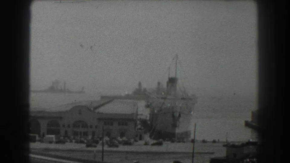 San Francisco waterfront in 1939 with a large ship beside the pier, distant vessels on the bay, and a hazy skyline area.