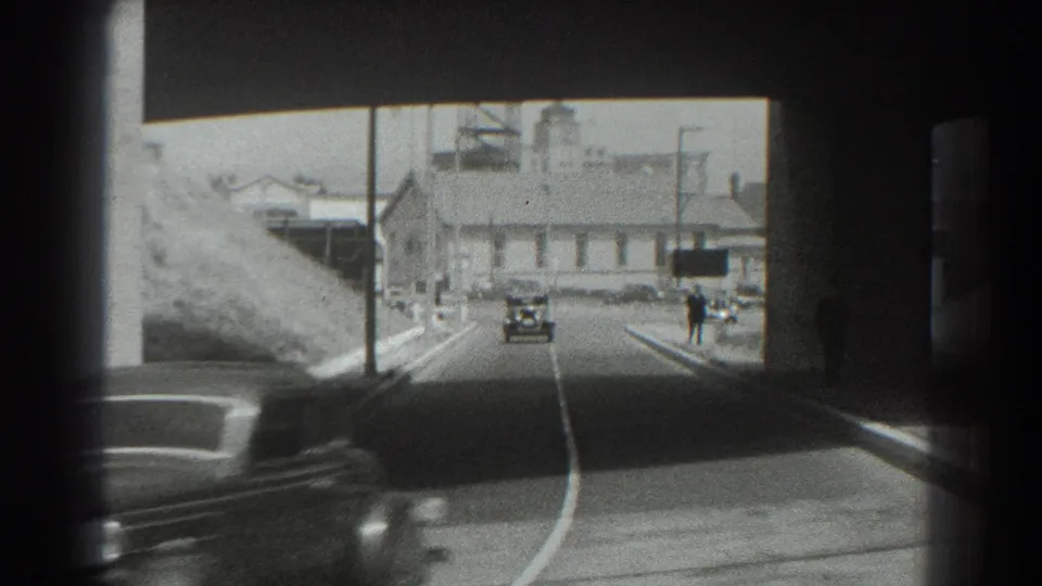 1939 San Francisco underpass frame with one car receding ahead and a blurred vehicle crossing the lower foreground near the bridge shadow.