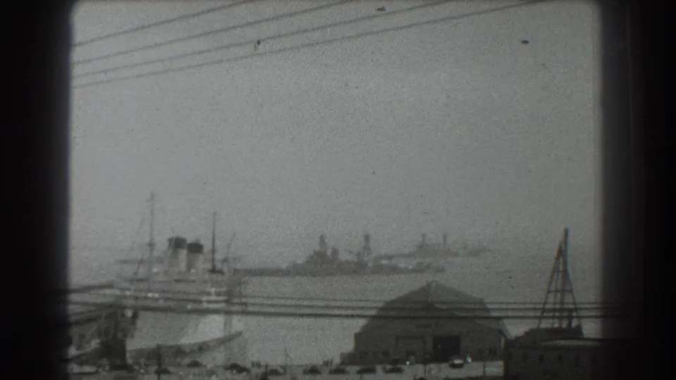 1939 San Francisco harbor view with ships on hazy water, dockside structures, overhead lines, and a dark foreground frame edge.