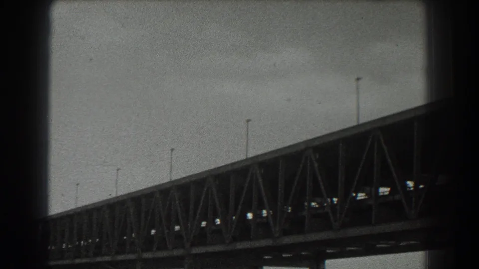 1939 San Francisco harbor view with a dark truss bridge span in the foreground and hazy water beyond.
