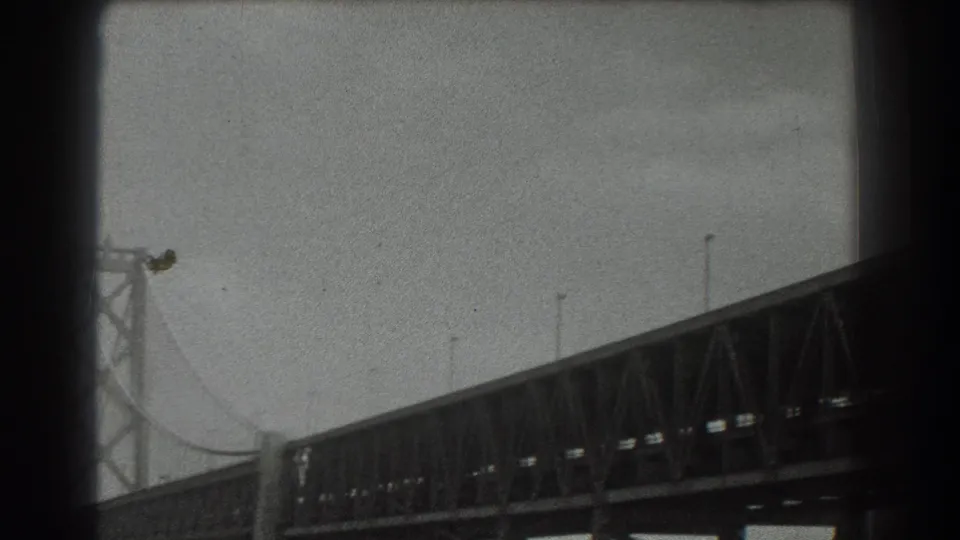 Black-and-white 1939 San Francisco frame with the Golden Gate Bridge span, tower detail, cables, and soft 8mm grain.