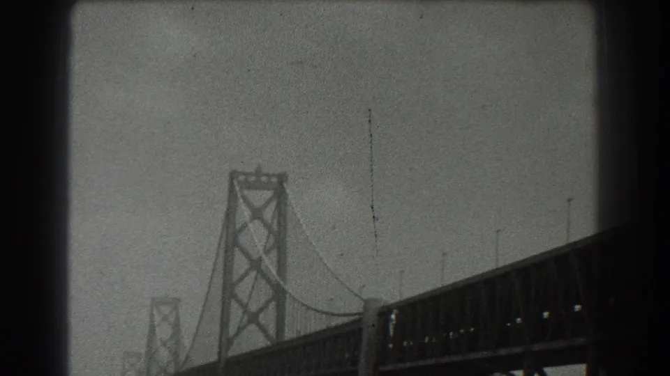 Late-1930s San Francisco home-movie frame with bridge tower, suspension cables, deck trusses, and visible 8mm film borders.