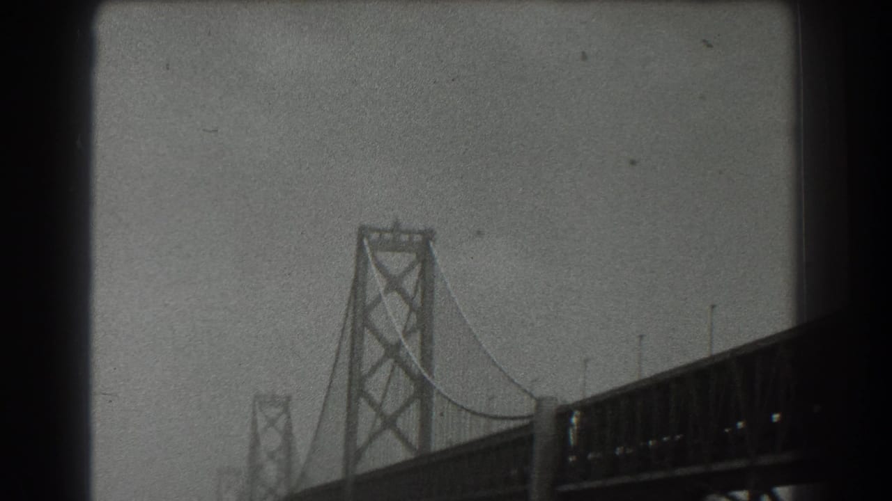 Close view of a suspension bridge tower and deck in hazy black-and-white film.